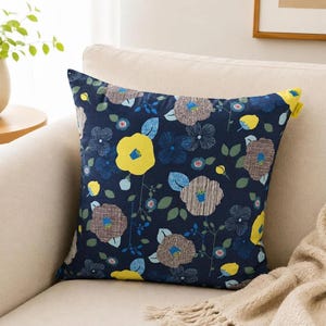 Könnte beinhalten: Ein quadratisches Zierkissen mit dunkelblauem Hintergrund und einem wiederkehrenden Blumenmuster. Das Design zeigt große gelbe Blüten, braun-weiß gestreifte kreisförmige Blüten, kleine blaue Blumen und grüne Blätter.