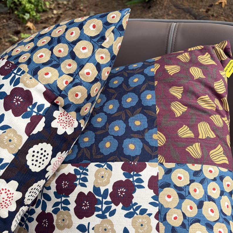 May include: Two square throw pillows featuring a patchwork design of various floral patterns. The fabrics include navy blue, cream, burgundy, and mustard yellow colors with prints of stylized flowers, petals, and circular botanical motifs.