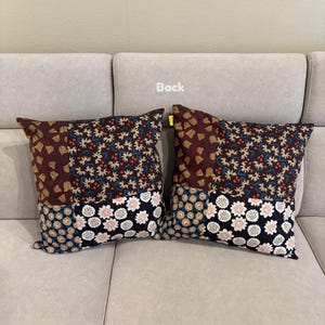 May include: Two square throw pillows featuring a patchwork design with four distinct fabric sections. The patterns include dark maroon with yellow shapes, a dense floral print, a blue and tan circular motif, and a black and white floral print.
