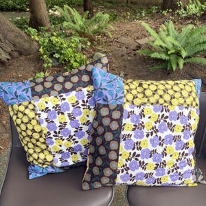 Peut inclure: Deux coussins carr&eacute;s pr&eacute;sentant un motif patchwork de fleurs dans des tons de jaune, violet, marron et blanc. Le tissu affiche des motifs r&eacute;p&eacute;titifs de petites fleurs et de feuilles dispos&eacute;s en sections rectangulaires distinctes sur la surface.