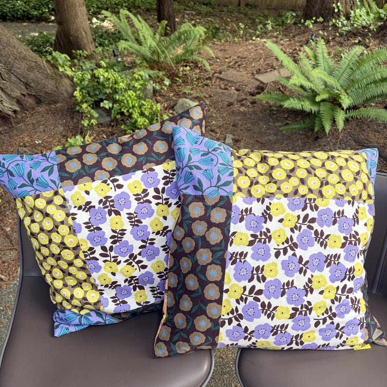 Peut inclure: Deux coussins carr&eacute;s pr&eacute;sentant un motif patchwork de fleurs dans des tons de jaune, violet, marron et blanc. Le tissu affiche des motifs r&eacute;p&eacute;titifs de petites fleurs et de feuilles dispos&eacute;s en sections rectangulaires distinctes sur la surface.