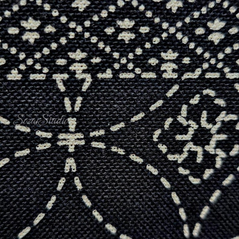 May include: A black fabric featuring a white stitched geometric pattern with repeating diamond and floral-like shapes. The embroidery consists of small, dashed lines creating a textured surface. The text Sozar Studio is visible in white.