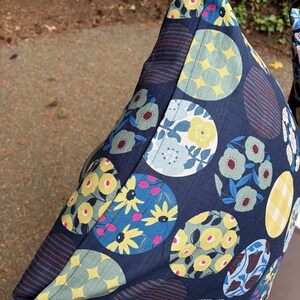 May include: A dark blue fabric pillow cover featuring a repeating pattern of circular motifs. The circles contain various designs including yellow flowers, light blue floral arrangements, yellow and white gingham checks, and dark red horizontal stripes.