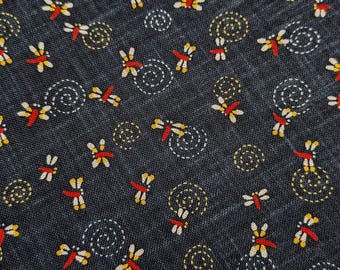 May include: A dark charcoal gray fabric featuring a repeating pattern of small dragonflies with red bodies and yellow wings, interspersed with white dotted spiral motifs that create a textured appearance across the entire surface of the material.