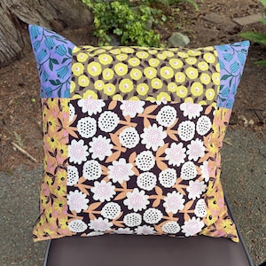 Peut inclure: Un coussin carr&eacute; pr&eacute;sentant un motif patchwork compos&eacute; de divers tissus &agrave; fleurs. Le panneau central affiche des fleurs blanches et roses sur fond marron fonc&eacute;, entour&eacute; de motifs floraux jaunes et de fleurs en cloche bleues aux coins.