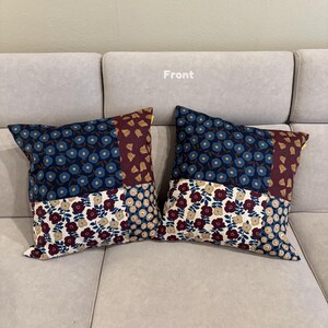 May include: Two square throw pillows featuring a patchwork design of floral patterns in navy blue, burgundy, and cream. The fabric displays repeating flower motifs across distinct sections, with the word Front printed in white above the pillows.