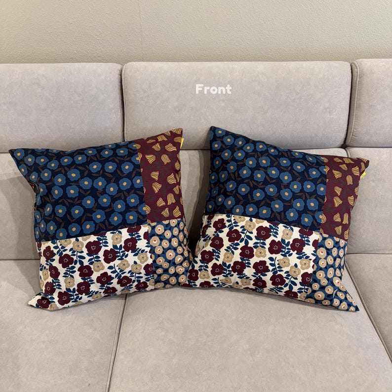 May include: Two square throw pillows featuring a patchwork design of floral patterns in navy blue, burgundy, and cream. The fabric displays repeating flower motifs across distinct sections, with the word Front printed in white above the pillows.