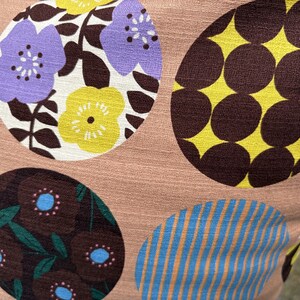 K&ouml;nnte beinhalten: Ein Stoff mit hellbraunem Hintergrund und gro&szlig;en kreisf&ouml;rmigen Mustern. Ein Kreis enth&auml;lt violette und gelbe Blumen auf wei&szlig;em Grund, ein anderer braune Punkte auf Gelb, einer zeigt braune Blumen mit blauen Zentren und einer hat blaue Streifen.