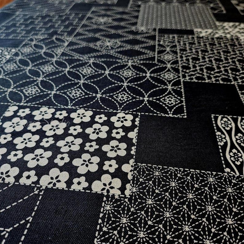 May include: A black fabric featuring a white patchwork design composed of various geometric and floral patterns. The textile displays repeating motifs including circles, stars, and blossoms arranged in a grid-like layout across the surface.