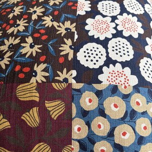 May include: A square textile panel featuring a patchwork design of four distinct floral patterns. The top left shows cream flowers on brown, top right white flowers on navy, bottom left yellow tulips on maroon, and bottom right beige flowers on blue.