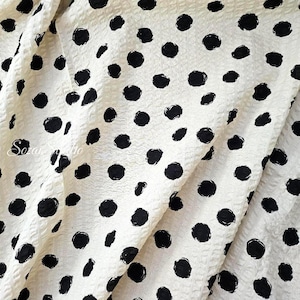 May include: Cream-colored fabric with a textured surface and a pattern of large, irregular black polka dots. The fabric is folded, creating soft shadows and highlighting the texture. The text "Soare Studio" is visible in the lower left corner.