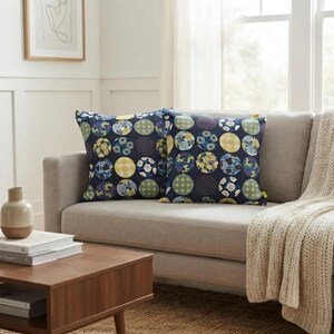 May include: Two square throw pillows featuring a dark navy blue background with a repeating pattern of large circles. Each circle contains different floral, gingham, or geometric prints in shades of yellow, blue, white, and green.