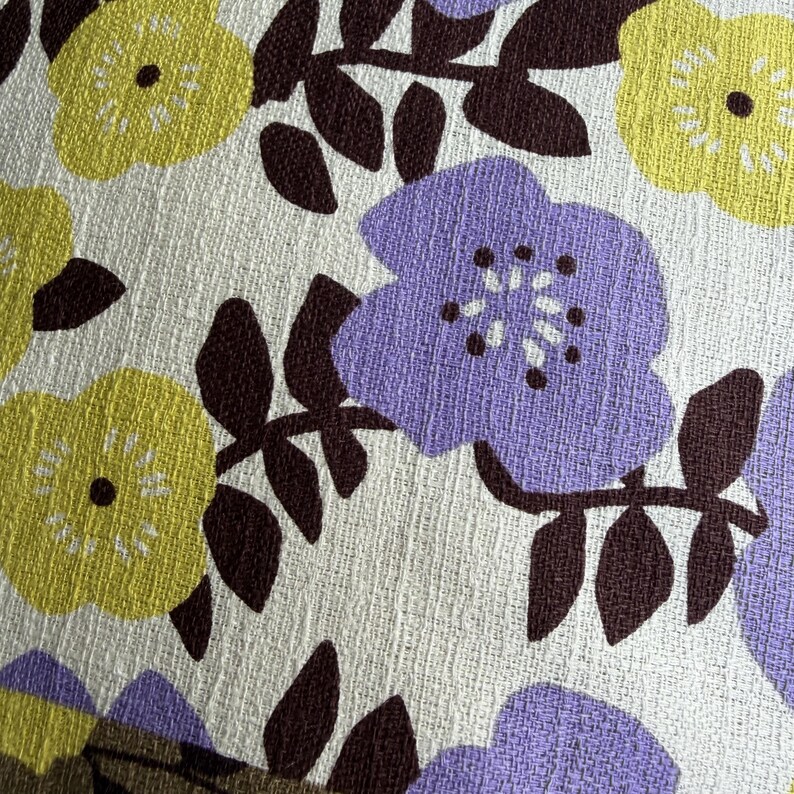 Peut inclure: Un tissu textile pr&eacute;sentant un motif floral r&eacute;p&eacute;titif sur fond blanc. Le design se compose de fleurs violet clair et vert citron avec des centres marron fonc&eacute;, accompagn&eacute;es de feuilles et de tiges marron fonc&eacute; sur une surface tiss&eacute;e textur&eacute;e.