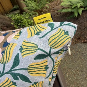 K&ouml;nnte beinhalten: Ein hellblauer Kissenbezug mit einem gewebten Muster aus gelben Tulpen mit dunkelgr&uuml;nen Stielen und Bl&auml;ttern. Am oberen Rand befindet sich ein kleines gelbes Stoffetikett mit der Aufschrift Atelier Dorothy Japanese Fabric und ein wei&szlig;er Rei&szlig;verschluss.
