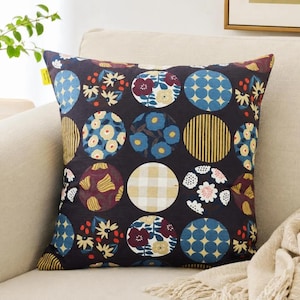 May include: A square throw pillow featuring a dark charcoal background with a repeating pattern of circles. Each circle contains distinct designs including blue and yellow flowers, yellow stripes, a beige gingham check, and blue polka dots.