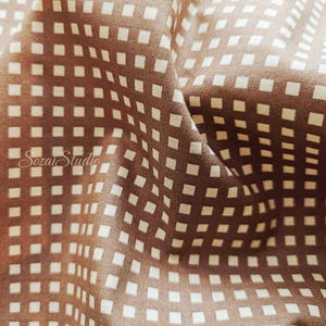 May include: Close-up of a brown fabric with a repeating pattern of small, off-white squares. The fabric is folded, creating shadows and highlighting the texture. The text "Sozai Studio" is visible in the lower left corner.