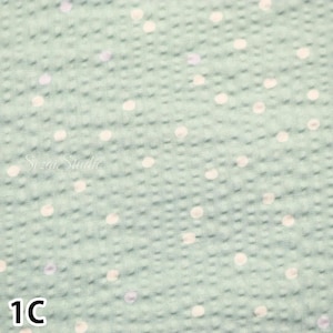 May include: Close-up of a light green fabric with a textured surface and scattered white polka dots. The number "1C" is printed in the bottom left corner. The words "Suzie Studio" are printed in the center.