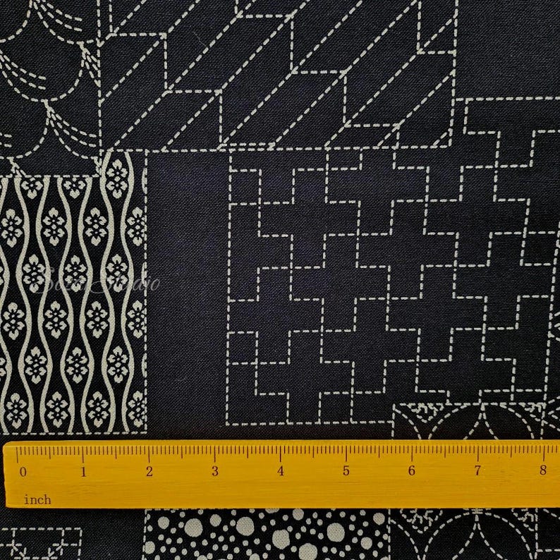 May include: A dark navy blue fabric featuring a white geometric sashiko-style stitched pattern with various repeating motifs including floral waves, squares, and dots. A yellow ruler is placed at the bottom, showing a length of 8 inches.