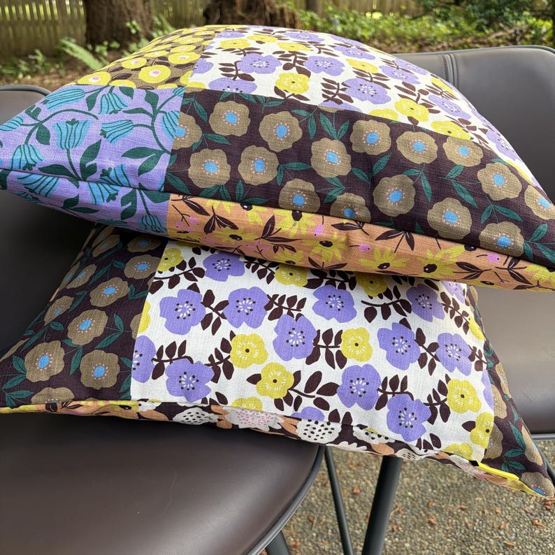 Peut inclure: Deux coussins carr&eacute;s pr&eacute;sentant un motif patchwork de fleurs. Le tissu affiche diverses sections avec des fonds marron, jaune, violet clair et blanc, d&eacute;cor&eacute;es de motifs floraux stylis&eacute;s dans des couleurs contrastantes.