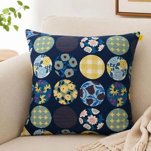 May include: A square throw pillow featuring a dark navy blue background with a repeating grid of circular patterns. Each circle displays a unique design, including yellow gingham, blue and yellow floral motifs, and geometric shapes in shades of blue, yellow, and white.