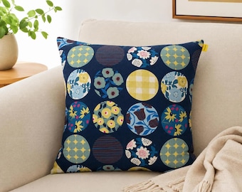 Peut inclure: Un coussin carré avec un fond bleu marine foncé orné d'une grille répétitive de motifs circulaires. Chaque cercle présente un design unique, incluant des motifs vichy jaunes, des fleurs bleues et jaunes, ainsi que des formes géométriques variées.