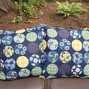 May include: Two square throw pillows featuring a dark navy blue background with a repeating pattern of circles. Each circle contains distinct designs including yellow gingham, blue and yellow floral prints, and geometric star or striped motifs.