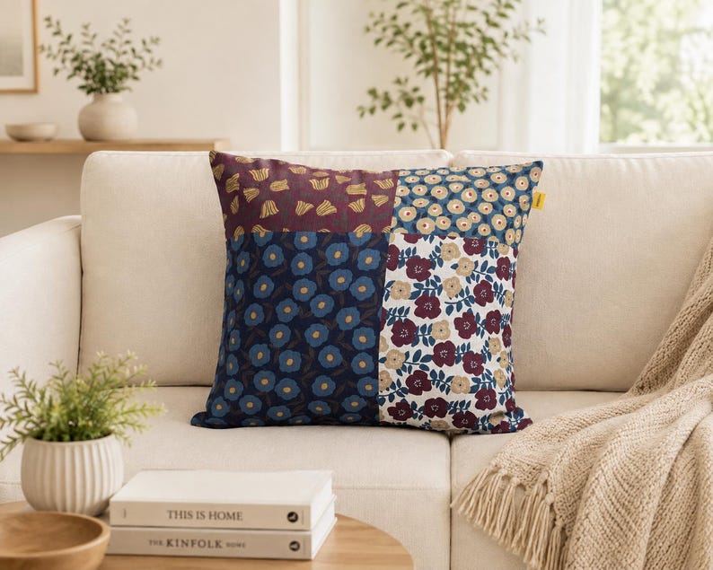 May include: A square throw pillow featuring a patchwork design composed of four distinct floral patterns. The sections display motifs of small yellow flowers on maroon, blue flowers on navy, light flowers on blue, and maroon flowers on white.