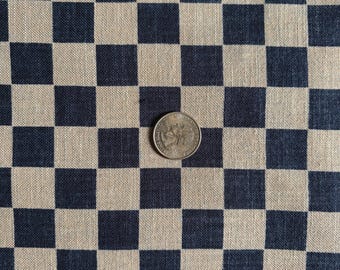 May include: A woven fabric featuring a repeating checkerboard pattern in dark navy blue and natural beige squares. A United States quarter coin is placed in the center of the fabric to provide a scale reference for the size of the individual squares.