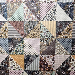 May include: A patchwork quilt with a variety of floral, dotted, and striped fabric patterns in a mix of colors including blue, pink, yellow, and gray. The quilt is made up of numerous triangular and square pieces sewn together.