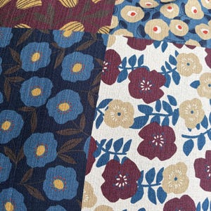 May include: A textile fabric featuring a patchwork design of floral patterns. The sections display blue flowers with yellow centers on a dark blue background, and maroon and beige flowers with blue leaves on a white and blue background.