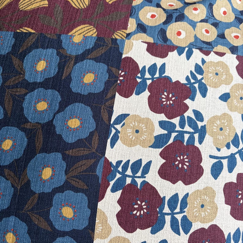 May include: A textile fabric featuring a patchwork design of floral patterns. The sections display blue flowers with yellow centers on a dark blue background, and maroon and beige flowers with blue leaves on a white and blue background.