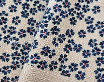May include: A beige fabric featuring a repeating pattern of small dark blue flowers with tiny red centers. The textile has a visible woven texture and includes the white cursive text Sozai Studio printed on the left side of the material.