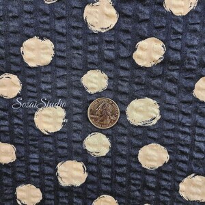 May include: Close-up of a textured fabric with a dark blue background and large, cream-colored polka dots. A quarter coin is included for scale. The fabric has a grid-like pattern. The text "Sozai Studio" is in the lower left corner.