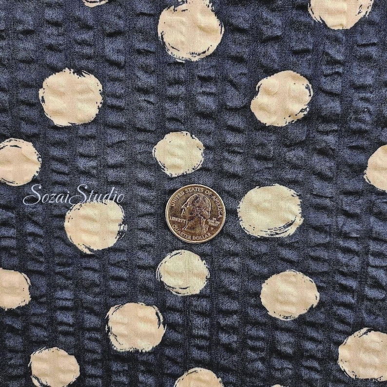May include: Close-up of a textured fabric with a dark blue background and large, cream-colored polka dots. A quarter coin is included for scale. The fabric has a grid-like pattern. The text "Sozai Studio" is in the lower left corner.