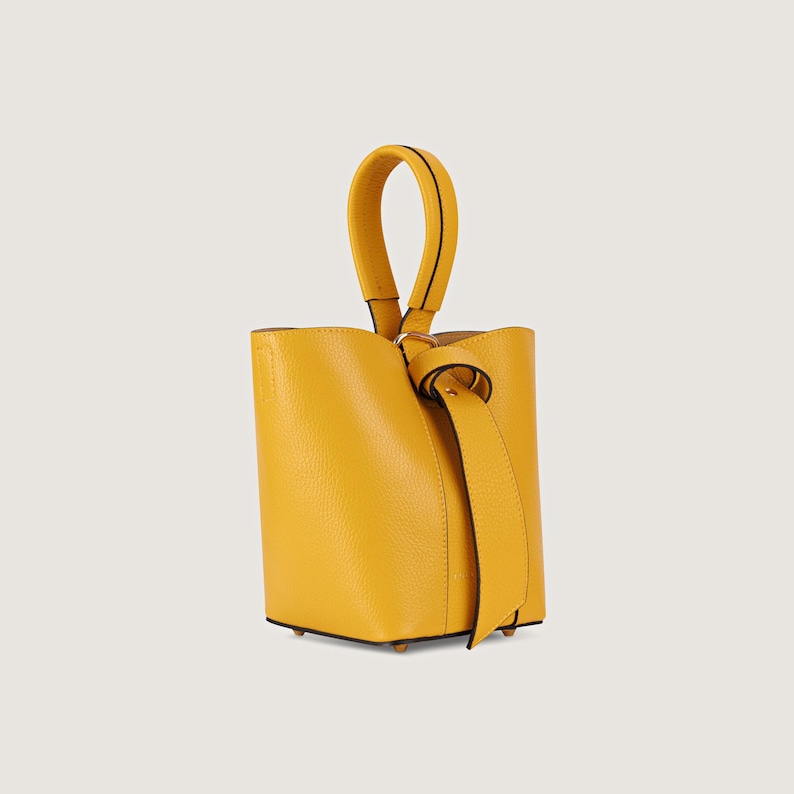 May include: A small, yellow leather bucket bag with a top handle and a knotted strap.
