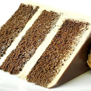 Puede incluir: Una rebanada de pastel de chocolate con capas de pastel de chocolate y glaseado blanco. El pastel está cubierto con una ganache de chocolate y un remolino de crema de mantequilla con sabor a café.