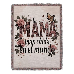 May include: A woven throw blanket with a floral design and the text "la mama mas chida en el mundo" in brown lettering. The letters are made up of floral patterns. A butterfly is in the top right corner.