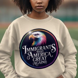 May include: A beige sweatshirt with a colorful graphic of an eagle with the text "Immigrants Make America Great (Again)"