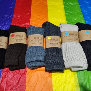 May include: Eight pairs of alpaca socks in various colors, including black, brown, gray, and white. The socks are folded and arranged on a rainbow-colored background. Each pair has a brown tag with the text "Choice Alpaca Socks Naturally Warm and Comfortable Alpaca Socks".