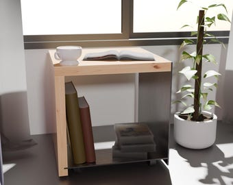 Puede incluir: Una mesa auxiliar de madera con un estante de vidrio. La mesa tiene una taza blanca y un libro en el estante superior. Hay libros en el estante inferior y una planta en una maceta blanca a la derecha de la mesa.