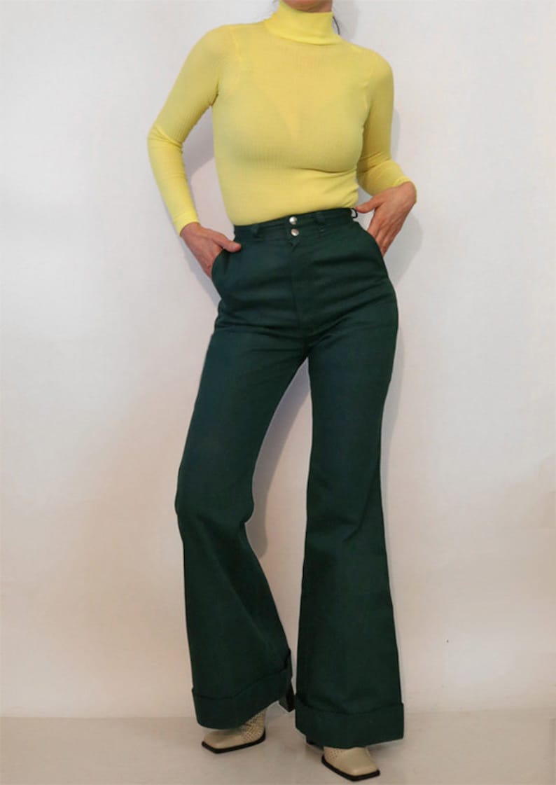 Puede incluir: Una mujer lleva un jersey de cuello alto amarillo brillante y pantalones anchos de color verde oscuro de cintura alta.