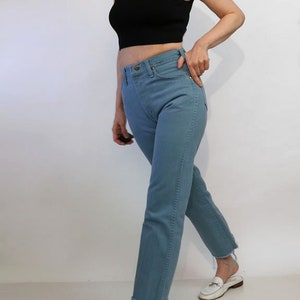 May include: A person wearing a black sleeveless turtleneck top and light blue jeans. The jeans have a raw hem and the person is wearing white loafers.