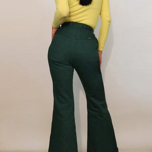 Puede incluir: Un par de pantalones de campana de pierna ancha, de cintura alta, de color verde oscuro con dobladillo vuelto. Los pantalones tienen un bolsillo trasero con una peque&ntilde;a etiqueta.