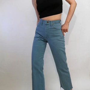 May include: A woman is wearing a black mock neck shirt and blue denim jeans with a raw hem. She is wearing white loafers.