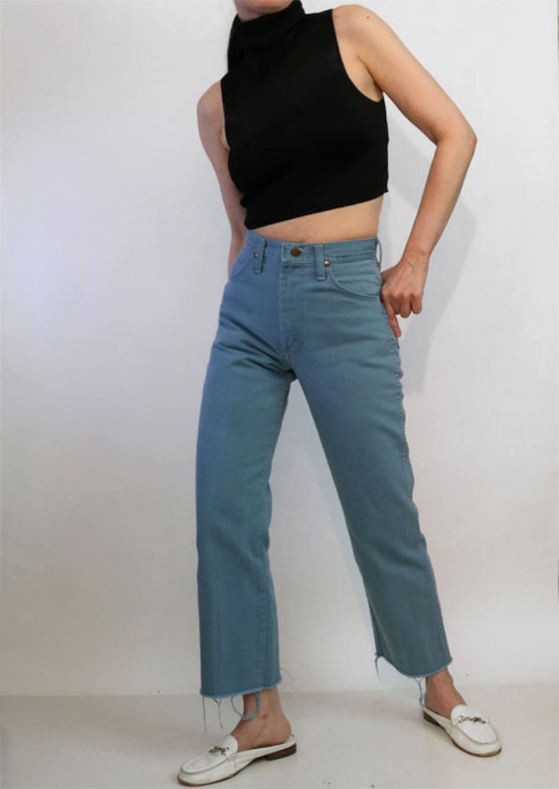 May include: A woman is wearing a black mock neck shirt and blue denim jeans with a raw hem. She is wearing white loafers.