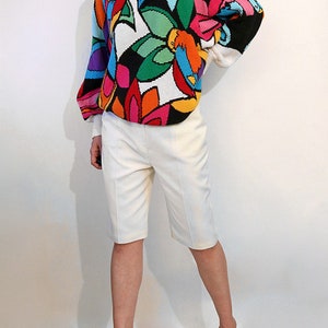 Puede incluir: Un su&eacute;ter blanco con un estampado floral abstracto de colores. El su&eacute;ter tiene mangas largas y un cuello redondo.