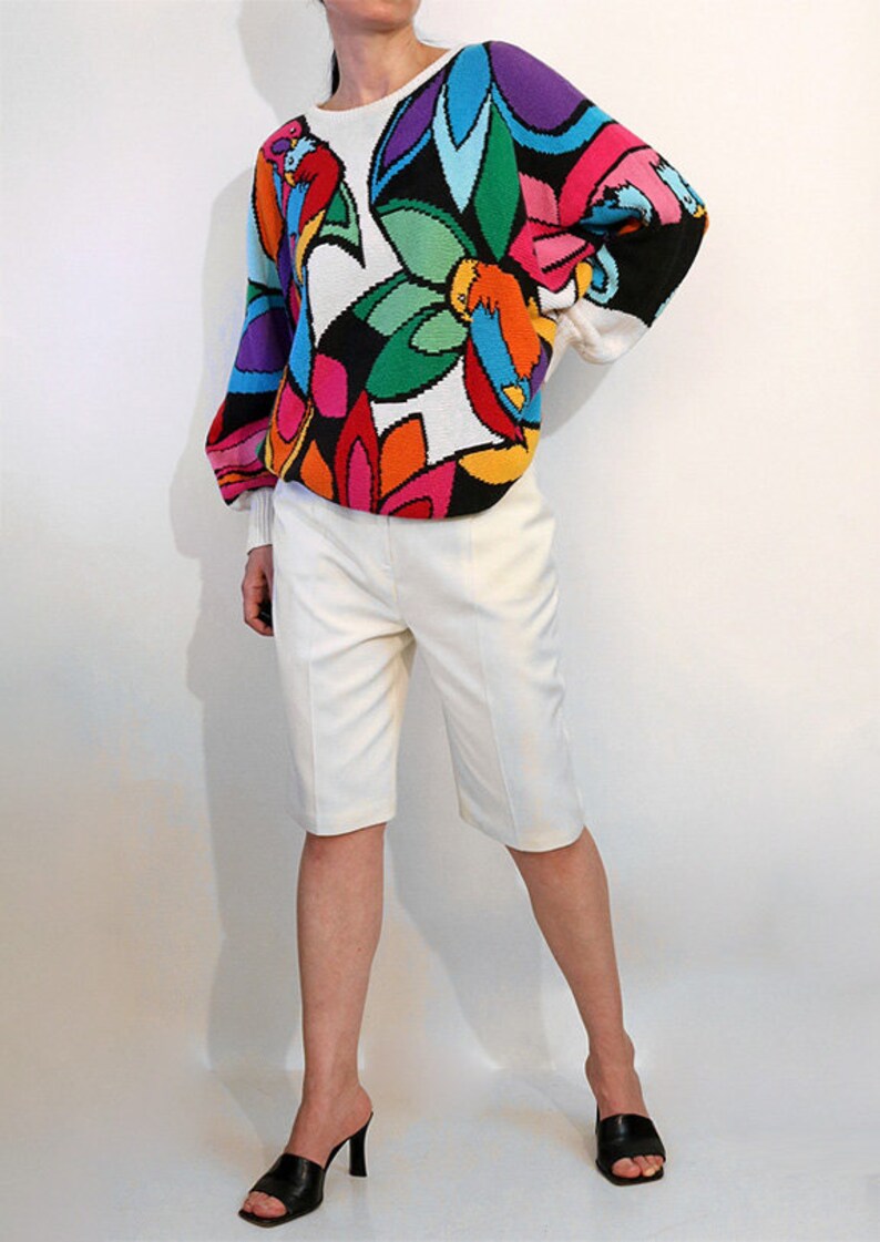 Puede incluir: Un su&eacute;ter blanco con un estampado floral abstracto de colores. El su&eacute;ter tiene mangas largas y un cuello redondo.
