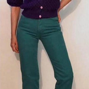 Puede incluir: Una persona con una rebeca morada con botones rosas y vaqueros verde azulado. La rebeca tiene mangas cortas. Los vaqueros son de color s&oacute;lido y tienen un corte recto.
