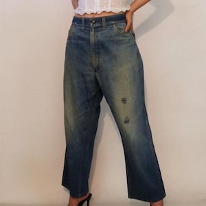 May include: A person wearing a white crop top and blue denim jeans with distressed details. The jeans have a wide leg and a high waist.