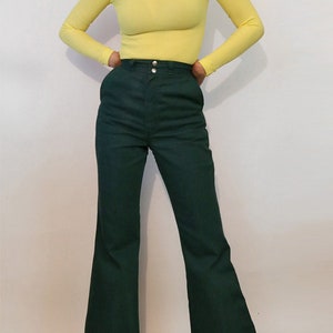 Puede incluir: Una mujer lleva un jersey de cuello alto amarillo brillante y pantalones anchos de color verde oscuro con dobladillo.
